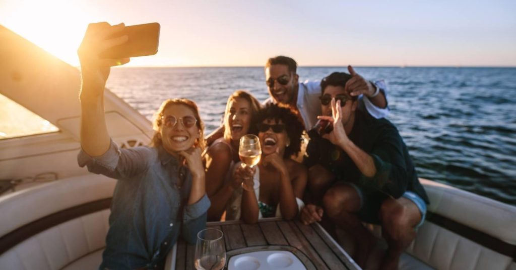 Group of happy friends taking a selfie and celebrating on a yacht charter during sunset