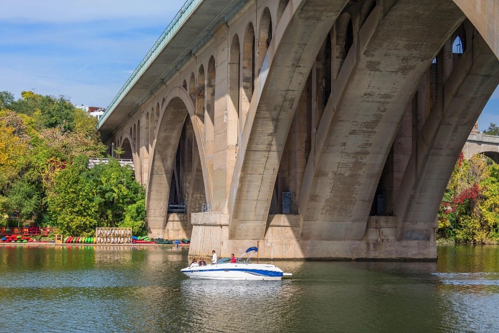 Small motorboat cruising near the stone arches of Francis Scott Key Bridge in Georgetown
